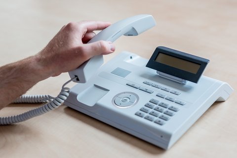 Eine Hand legt einen Hörer auf ein Telefon.